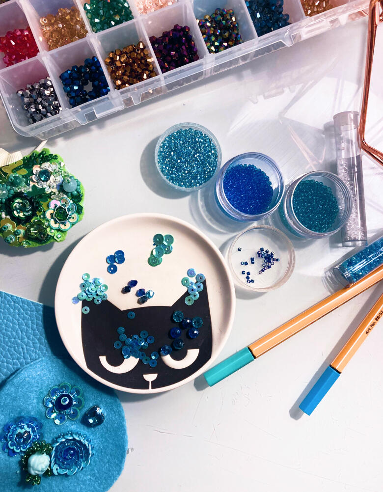 Beads, sequins and a cat-shaped dish on Olya's workspace